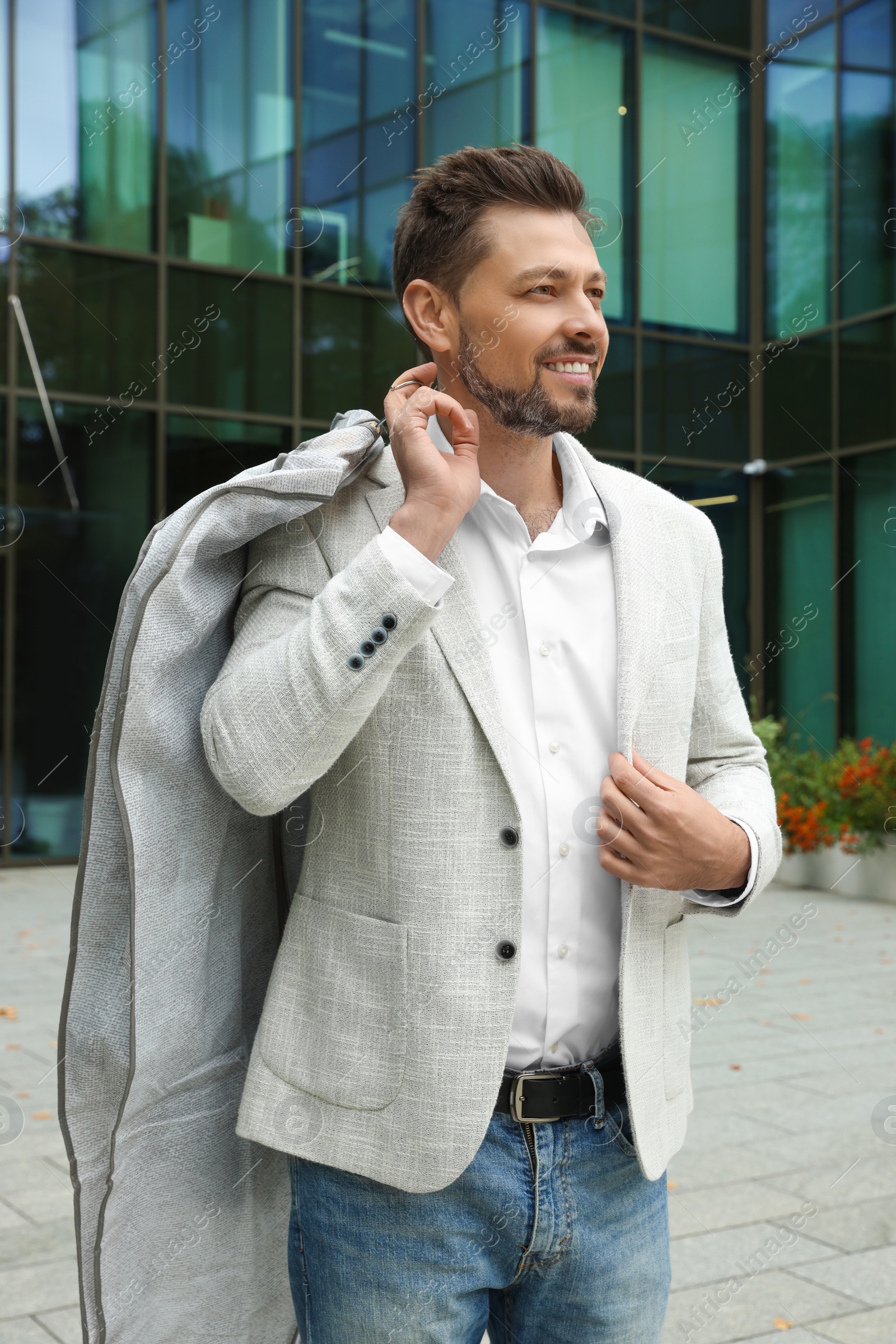 Photo of Attractive happy man holding garment cover with clothes outdoors. Dry cleaning service