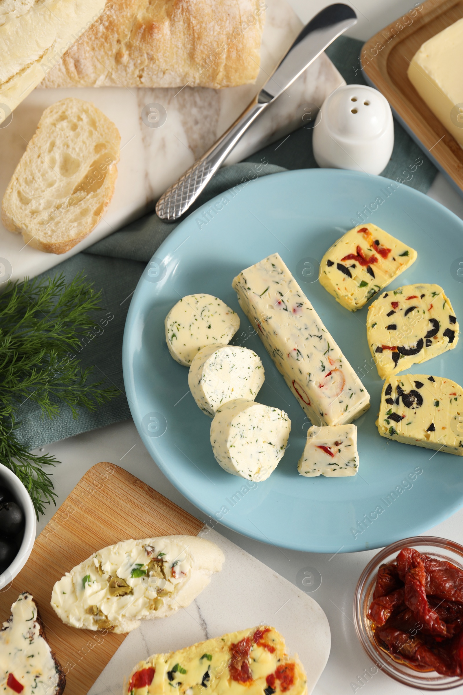 Photo of Different types of tasty butter, dill, chili peppers and bread on white table, flat lay