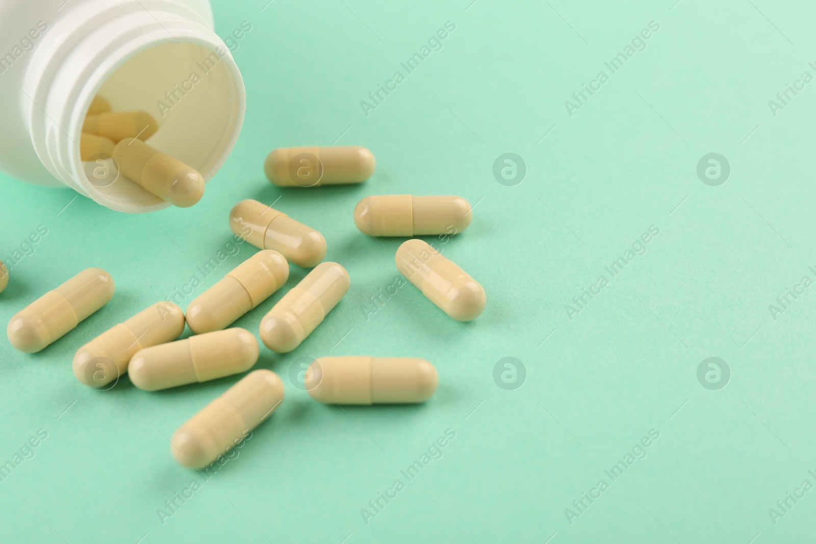 Photo of Bottle and vitamin capsules on turquoise background, closeup. Space for text