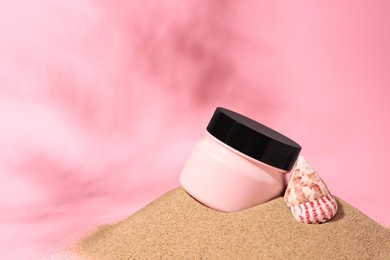 Photo of Jar of cream and seashell on sand against pink background. Space for text