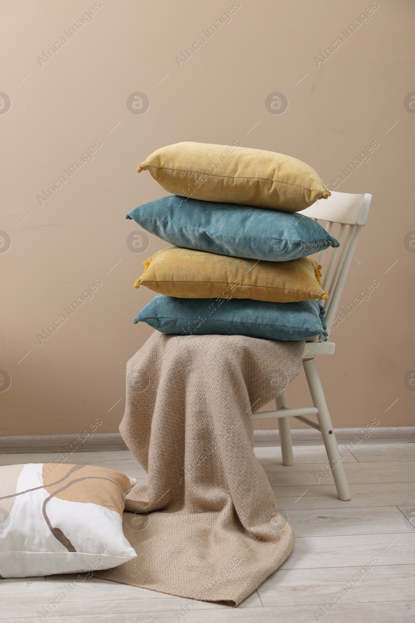 Photo of Soft pillows and warm blanket near beige wall indoors
