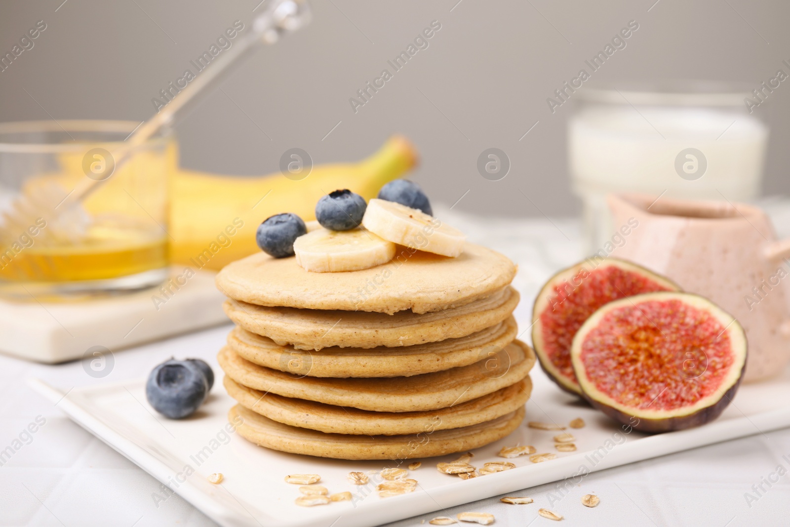 Photo of Tasty oatmeal pancakes on white tiled table, closeup