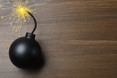 Image of Old fashioned black bomb with lit fuse on wooden table, top view. Space for text