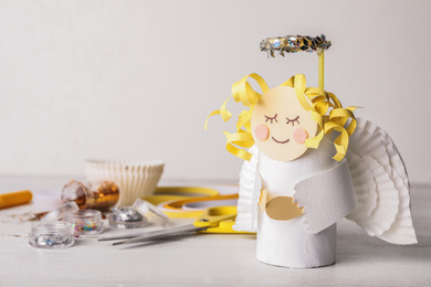Toy angel made of toilet paper hub on white wooden table. Space for text