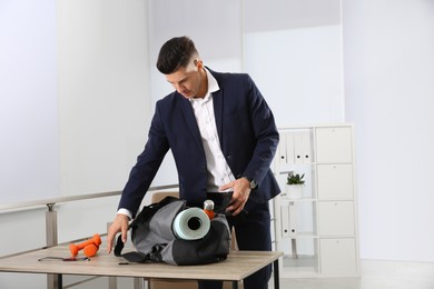 Businessman packing sports stuff for training into bag in office