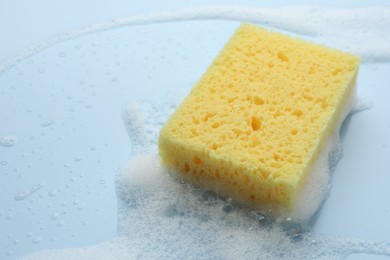 Yellow sponge with foam on light blue background, closeup