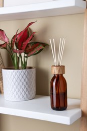 Photo of Aromatic reed air freshener near houseplant on wooden shelf