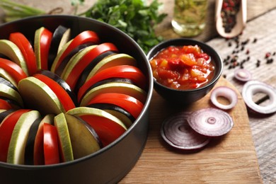 Photo of Cooking delicious ratatouille. Different fresh vegetables and round baking pan on wooden board, closeup