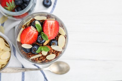 Photo of Tasty granola with berries, almond flakes and mint in glass on white table, flat lay. Space for text