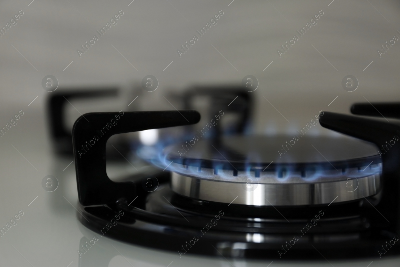 Photo of Gas burner with blue flame on modern stove, closeup