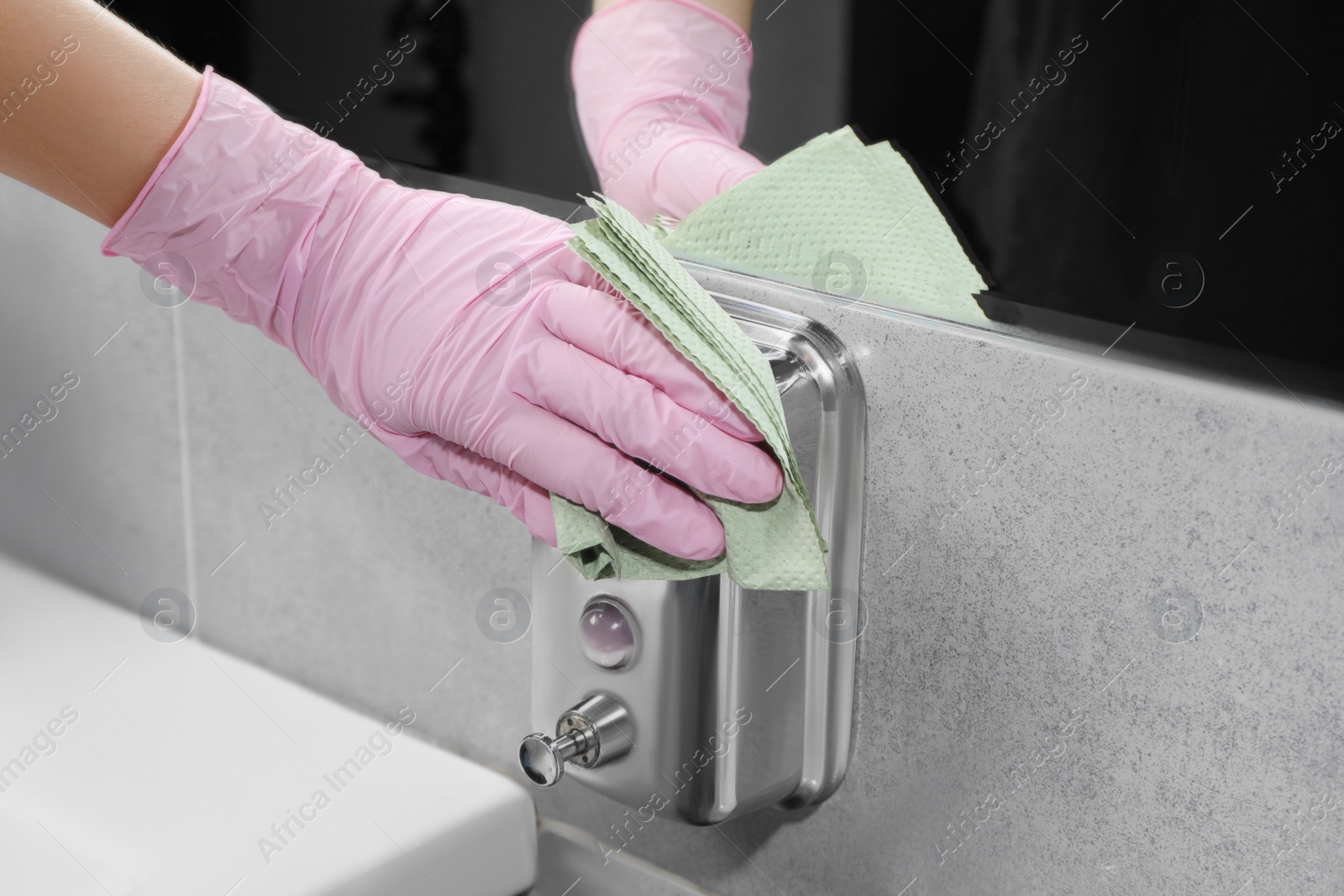 Photo of Woman in glove cleaning liquid soap dispenser with paper towel, closeup