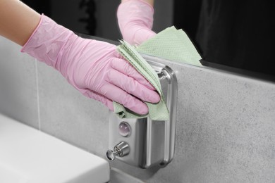 Photo of Woman in glove cleaning liquid soap dispenser with paper towel, closeup