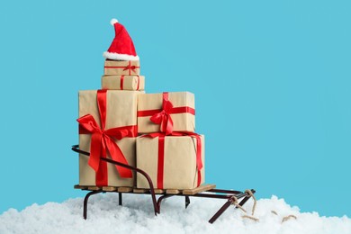 Photo of Sleigh with Christmas gift boxes, Santa hat and artificial snow on light blue background