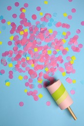 Photo of Party popper with bright confetti on light blue background, flat lay