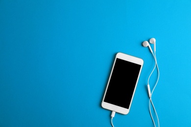 Photo of Modern phone with earphones on blue background, top view. Space for text