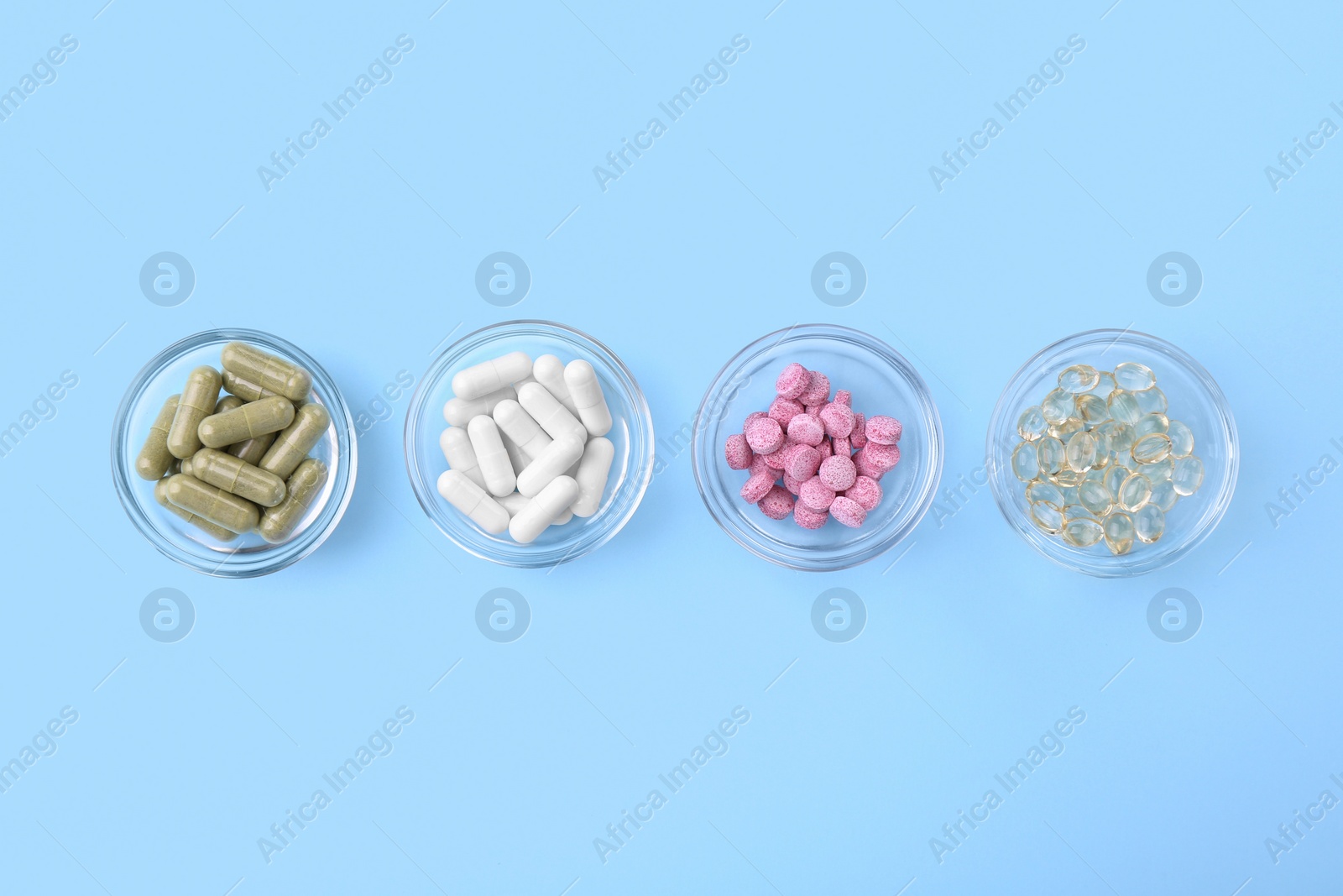 Photo of Different vitamin pills in bowls on light blue background, flat lay