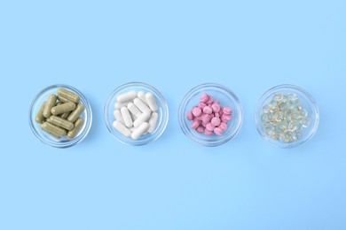 Different vitamin pills in bowls on light blue background, flat lay