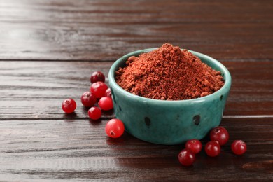 Photo of Dried cranberry powder in bowl and fresh berries on wooden table. Space for text