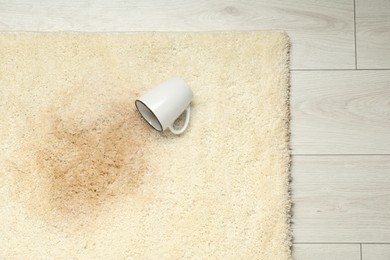 Photo of Overturned cup and spilled drink on beige carpet, top view. Space for text