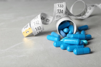 Weight loss pills, bottle and measuring tape on table