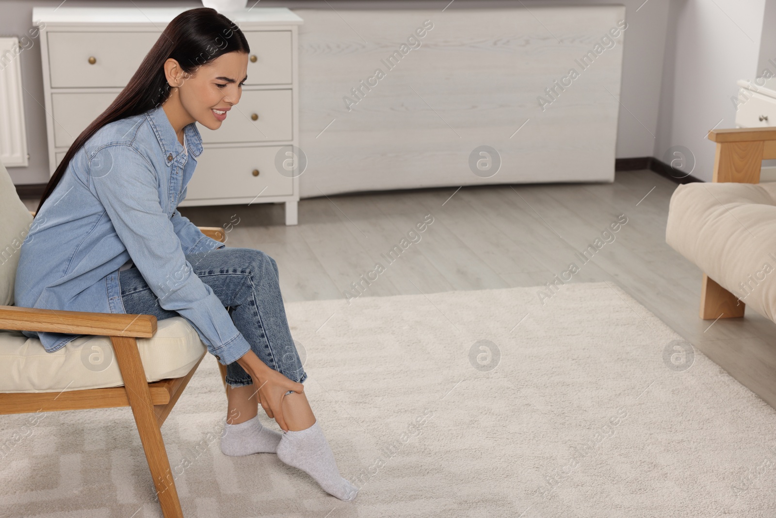 Photo of Woman suffering from leg pain on armchair at home, space for text