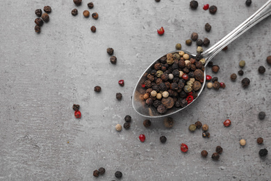 Photo of Spoon with mixed peppercorns on grey table, flat lay