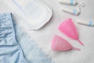 Photo of Woman's panties, menstrual pad, cups and tampons on white fabric, flat lay