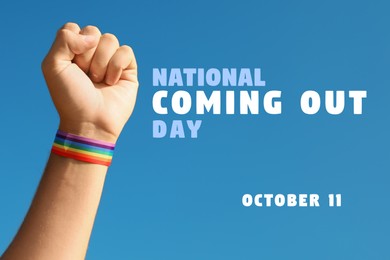 Image of National Coming Out day, October 11. Man wearing pride rainbow wristband on hand against blue sky, closeup