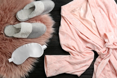 Photo of Flat lay composition with fluffy slippers and bath robe on black wooden background. Comfortable home outfit