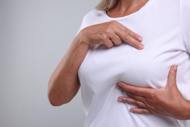 Woman doing breast self-examination on light grey background, closeup. Space for text