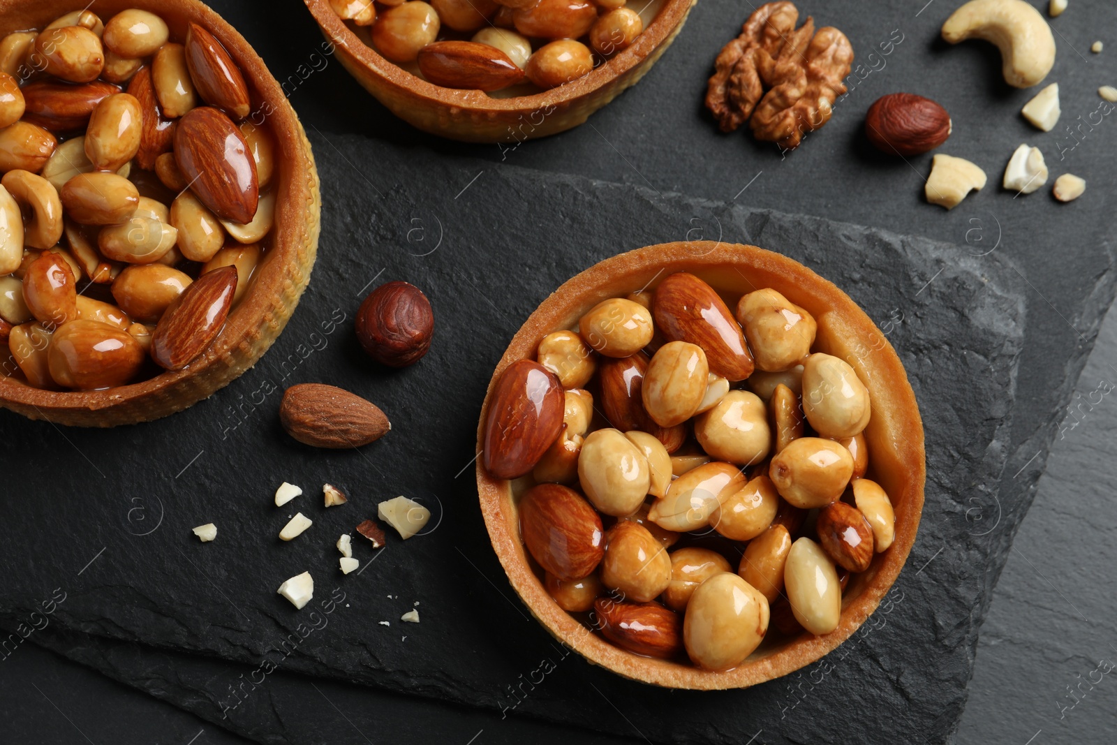 Photo of Tartlets with caramelized nuts on black table, top view. Delicious dessert