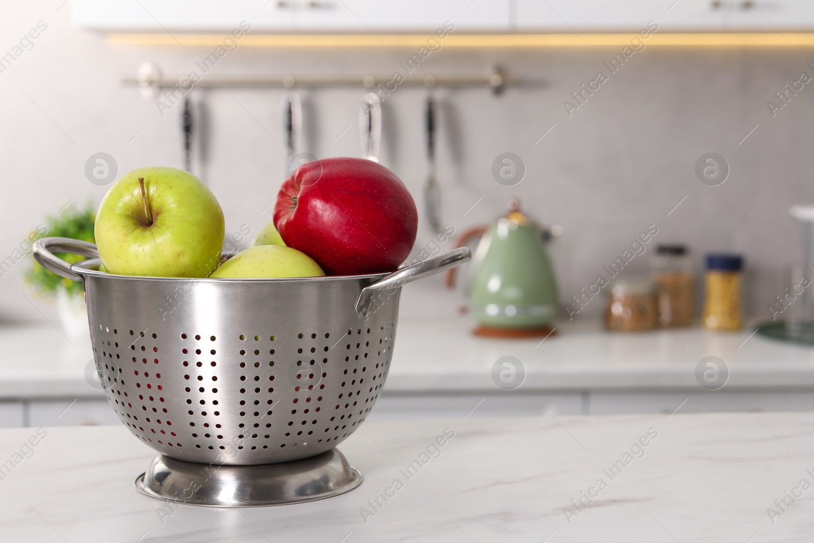 Photo of Colander with fresh apples on white marble table in kitchen. Space for text