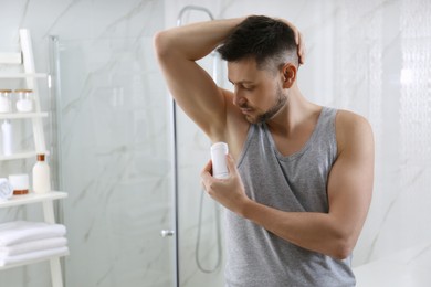 Photo of Handsome man applying deodorant in bathroom. Space for text