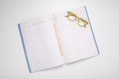 Open monthly planner, glasses and pencil on white background, top view