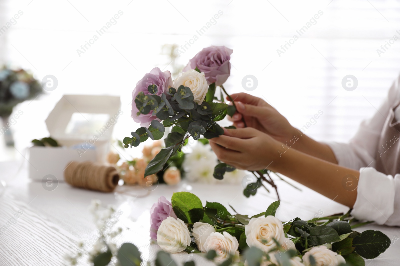 Photo of Florist making beautiful wedding bouquet at white table, closeup