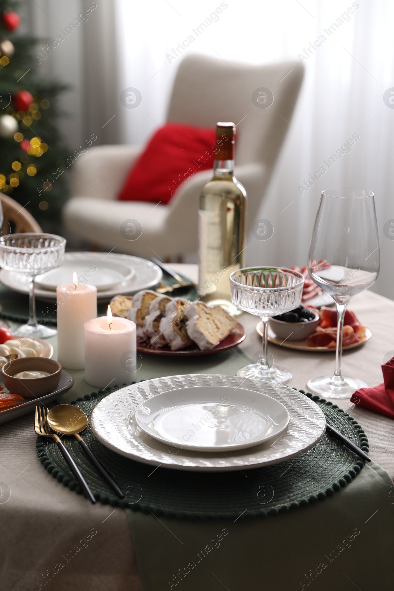 Photo of Christmas table setting with burning candles, appetizers and dishware indoors