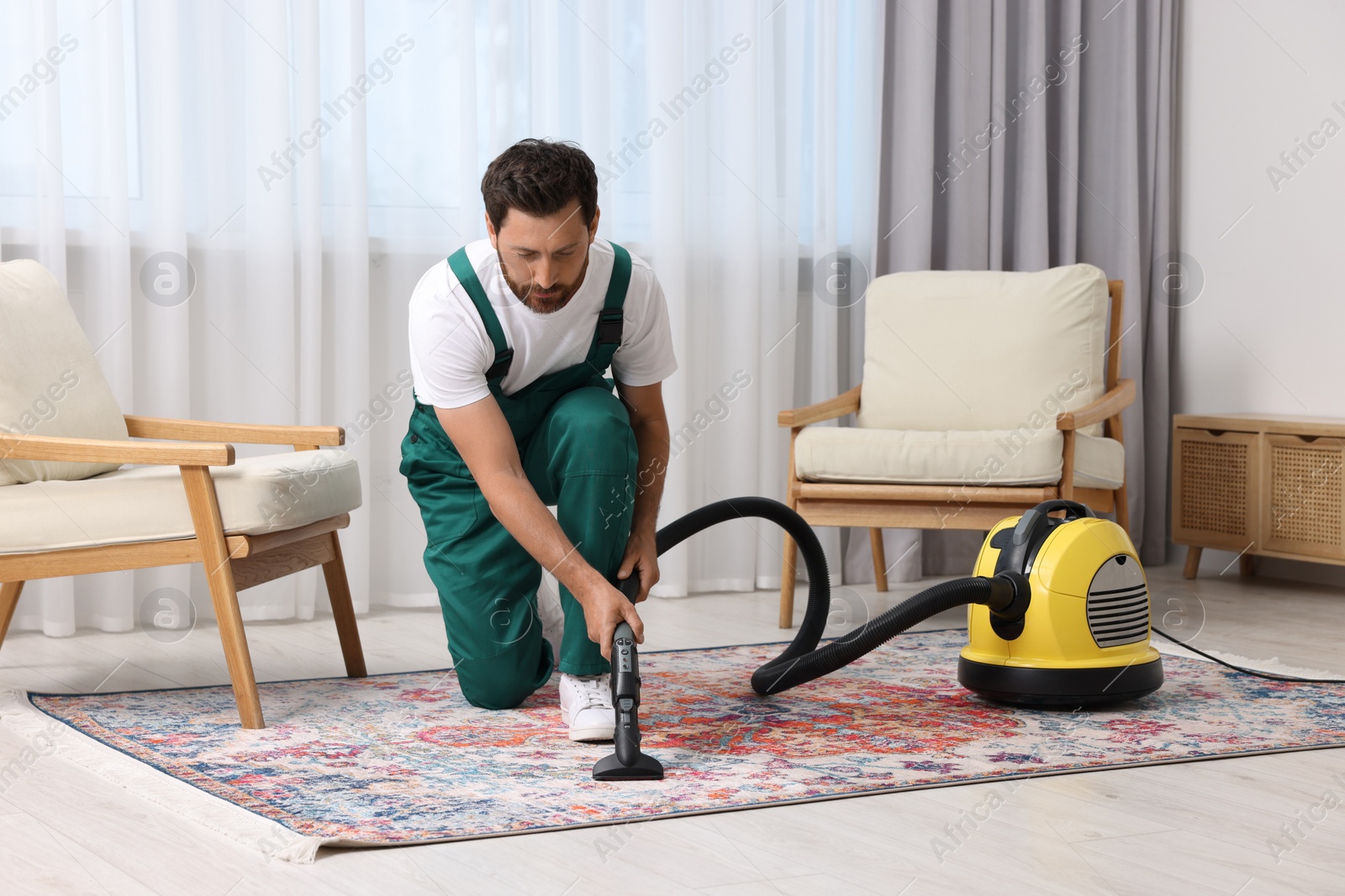 Photo of Dry cleaner's employee hoovering carpet with vacuum cleaner in room