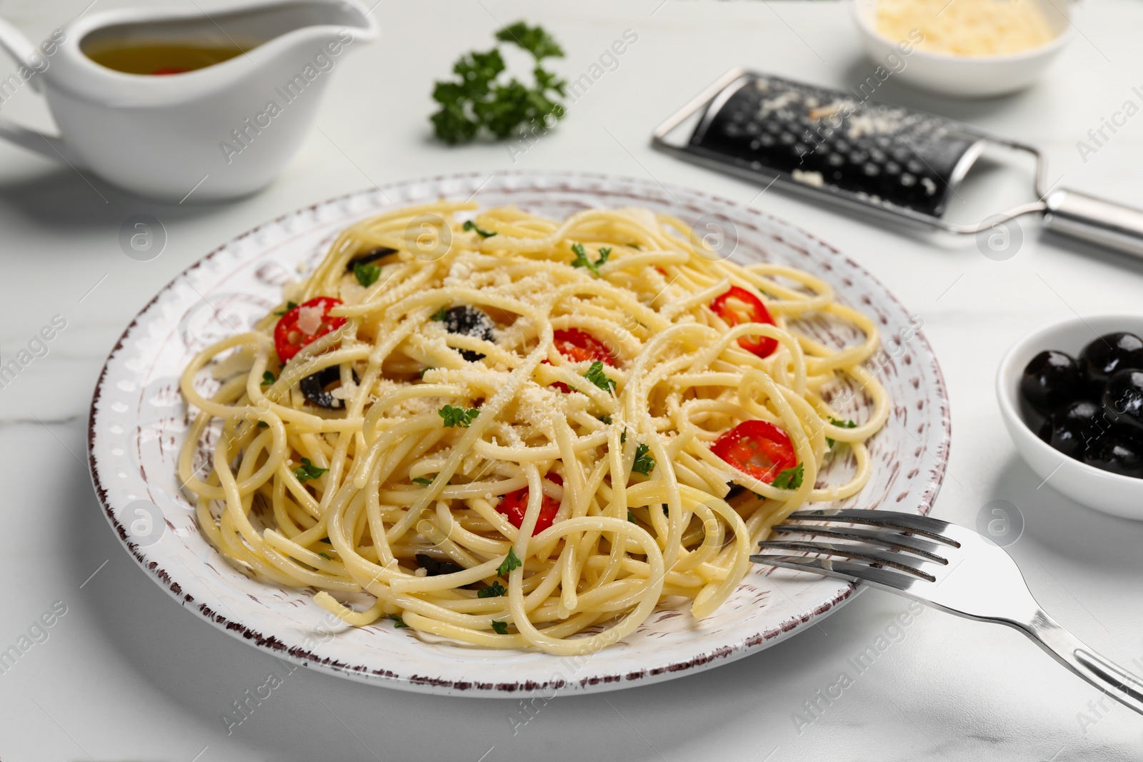 Photo of Delicious pasta with olives, tomatoes and parmesan cheese served on white marble table, closeup