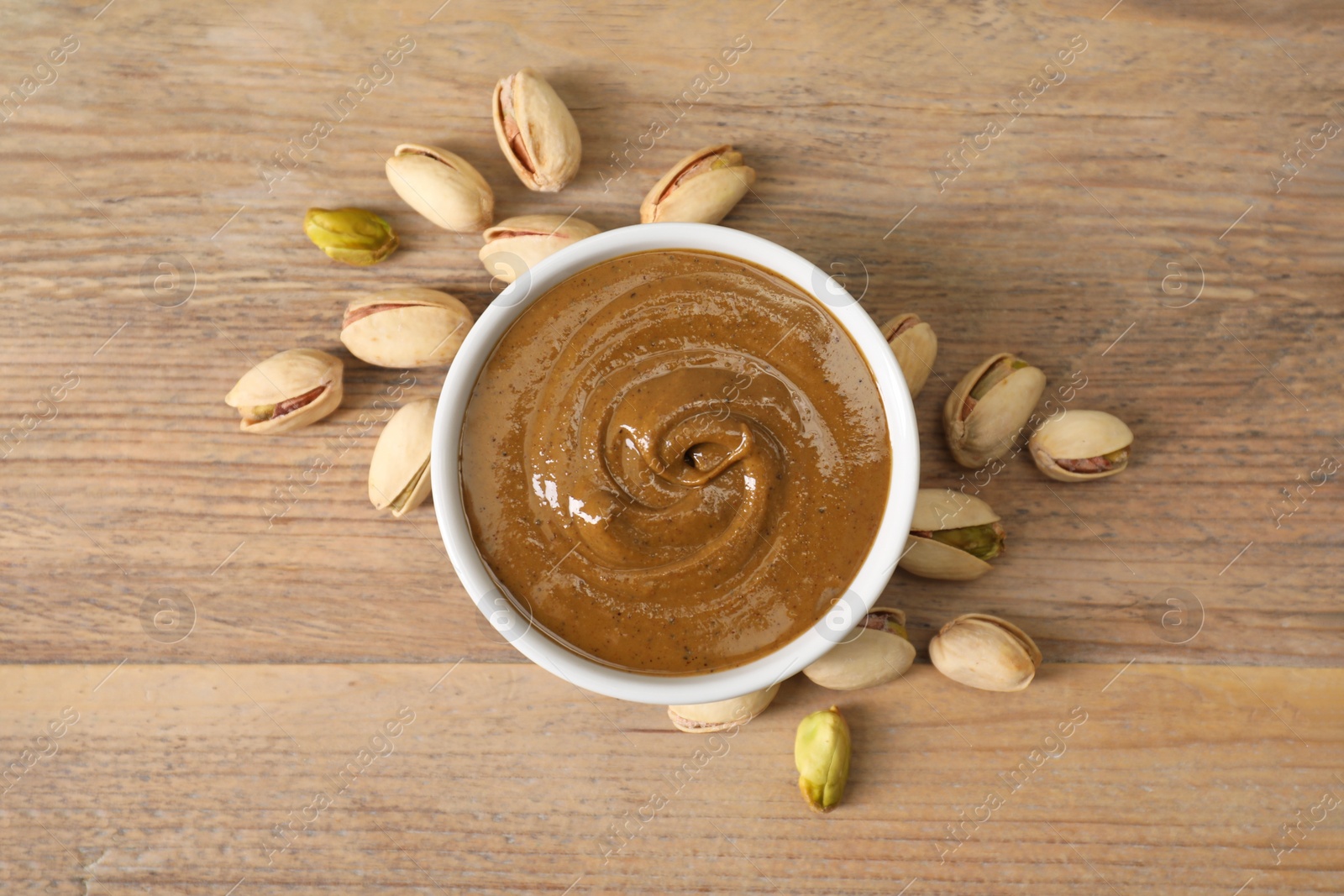 Photo of Delicious nut butter in bowl and pistachios on wooden table, top view