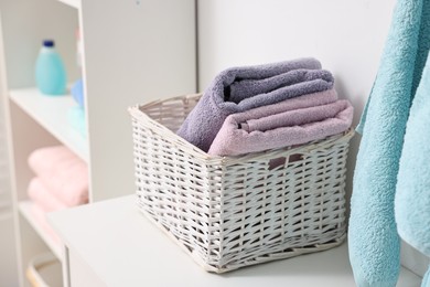Stacked fresh towels with laundry basket on table indoors