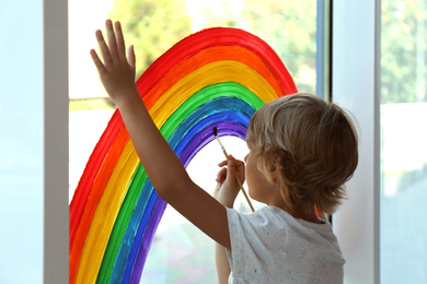 Photo of Little boy drawing rainbow on window. Stay at home concept