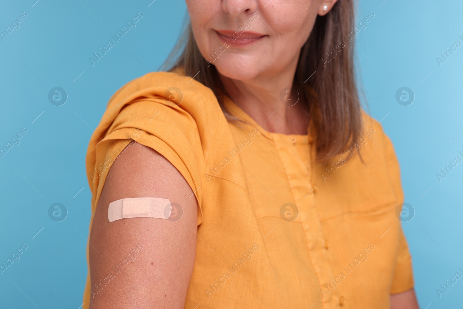 Photo of Woman with adhesive bandage on her arm after vaccination against light blue background, closeup
