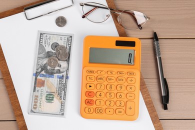Photo of Orange calculator, money, clipboard with paper sheet, pen and glasses on wooden table, flat lay. Retirement concept