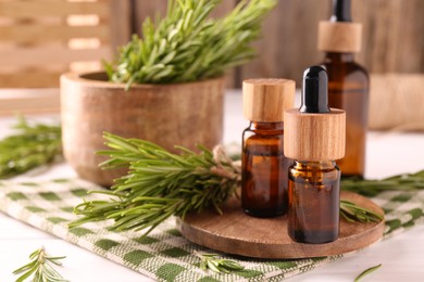 Photo of Essential oil in bottles and rosemary on white wooden table