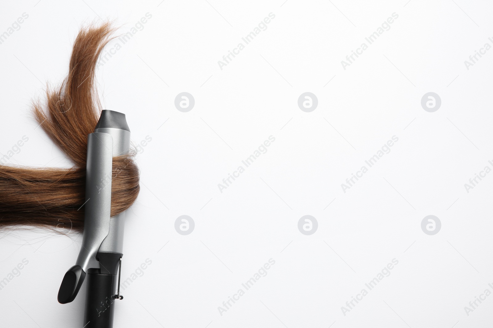 Photo of Curling iron with brown hair lock on white background, top view. Space for text