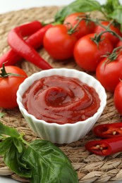 Bowl of tasty ketchup and ingredients on wicker mat, closeup