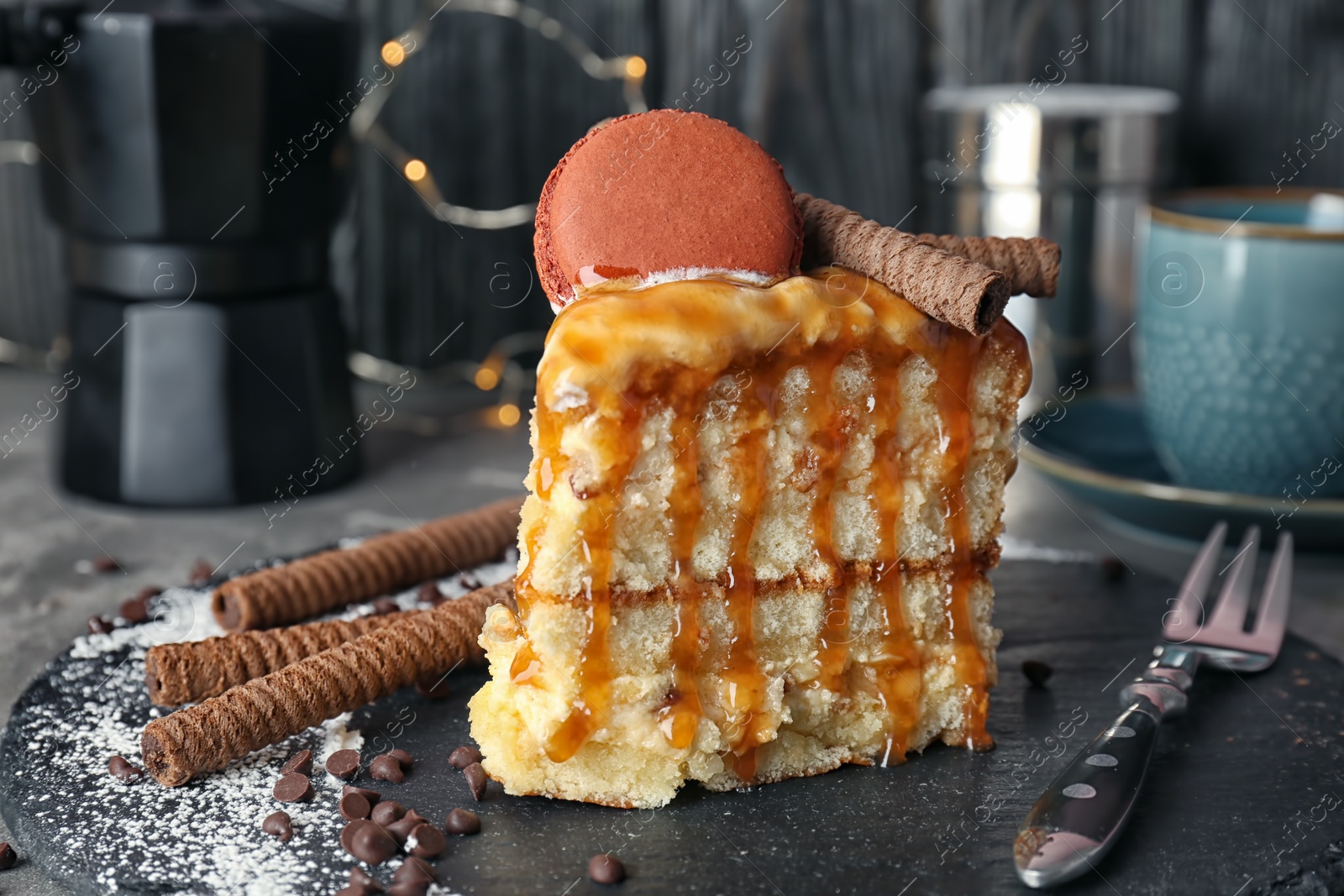 Photo of Piece of delicious homemade cake with caramel sauce and macaron on table