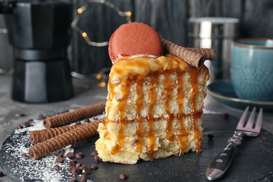 Photo of Piece of delicious homemade cake with caramel sauce and macaron on table