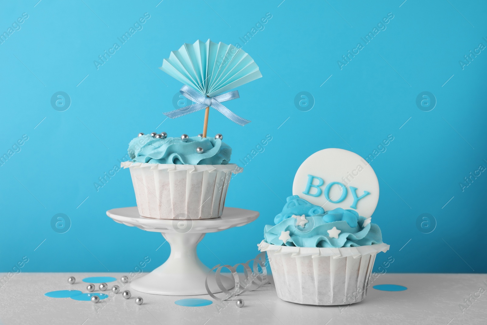 Photo of Baby shower cupcakes with toppers on white table against light blue background