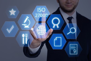 Image of Businessman pointing at virtual icon with text ISO 27000 on grey background, closeup 